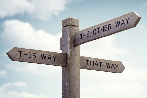 Coaching Essen, berufliche Entwicklung_Vor einem blauen, leicht bewölkten Himmel steht ein Wegweiser mit drei Richtungen, this way, that wax, the other way